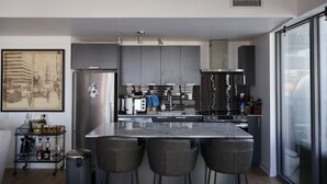 Een moderne keuken met een centraal eiland, barstoelen, een roestvrijstalen koelkast en een groot raam.