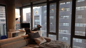 Een moderne woonkamer met een bank, een bureau en een groot raam met uitzicht op de stad.