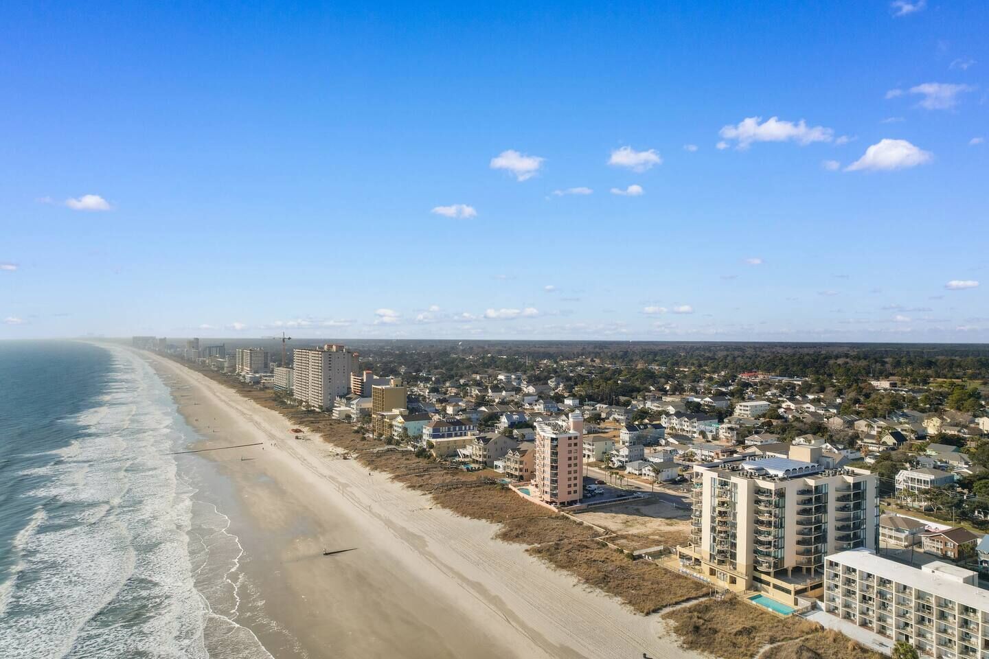 A coastal cityscape with a beach, high-rise buildings, and a clear sky.