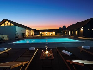 Ein Pool mit Liegestühlen und einem Tisch mit Getränken, umgeben von Gebäuden im Abenddämmerung.