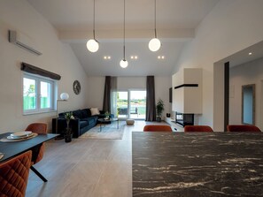 Ein modernes Wohnzimmer mit Sofa, Esstisch, Stühlen, Kamin und einem großen Fenster mit Blick.