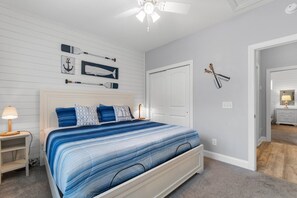 A bedroom with a bed, a nightstand, a lamp, a ceiling fan, and a door leading to another room. - Sea Coral Escape- Resort Pool, Private Home (North Myrtle Beach)