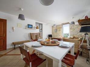 A dining area with a white table, red chairs, a wicker sofa, and a stone wall.