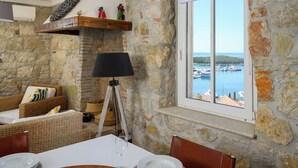 Une pièce aux murs de pierre, avec une table à manger, des meubles en osier, une lampe et une vue sur un port.