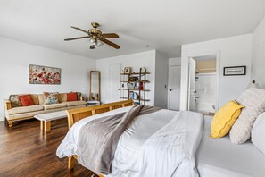 Ein Schlafzimmer mit Bett, Sofa, Sitzbank, Bücherregal und Deckenventilator.