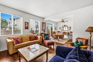 Ein Wohnzimmer mit einer Couch, einem Hocker, einem Couchtisch und einem Essbereich mit Stühlen und Tisch.