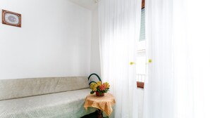 Une pièce avec un canapé, une petite table sur laquelle est posé un vase de fleurs, et une porte avec des rideaux.