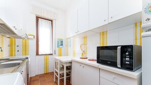 Une cuisine de taille réduite, équipée d’un four à micro-ondes, d’un évier et d’une fenêtre avec des rideaux.