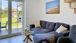 Ein Wohnzimmer mit Glastisch, grauem Sofa und einem Gemälde von einem Strand.