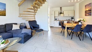 Ein modernes Wohnzimmer mit einem dunkelgrauen Sofa, einem Glastisch und einer Wendeltreppe, die in einen Küchenbereich führt.