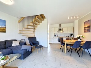 Una sala de estar moderna con un sofá gris oscuro, una mesa de centro de vidrio y una escalera de caracol que lleva a una zona de cocina.