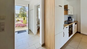 Eine moderne Küche mit weißen Schränken, einer Wand in Holzoptik und Blick durch die Tür.