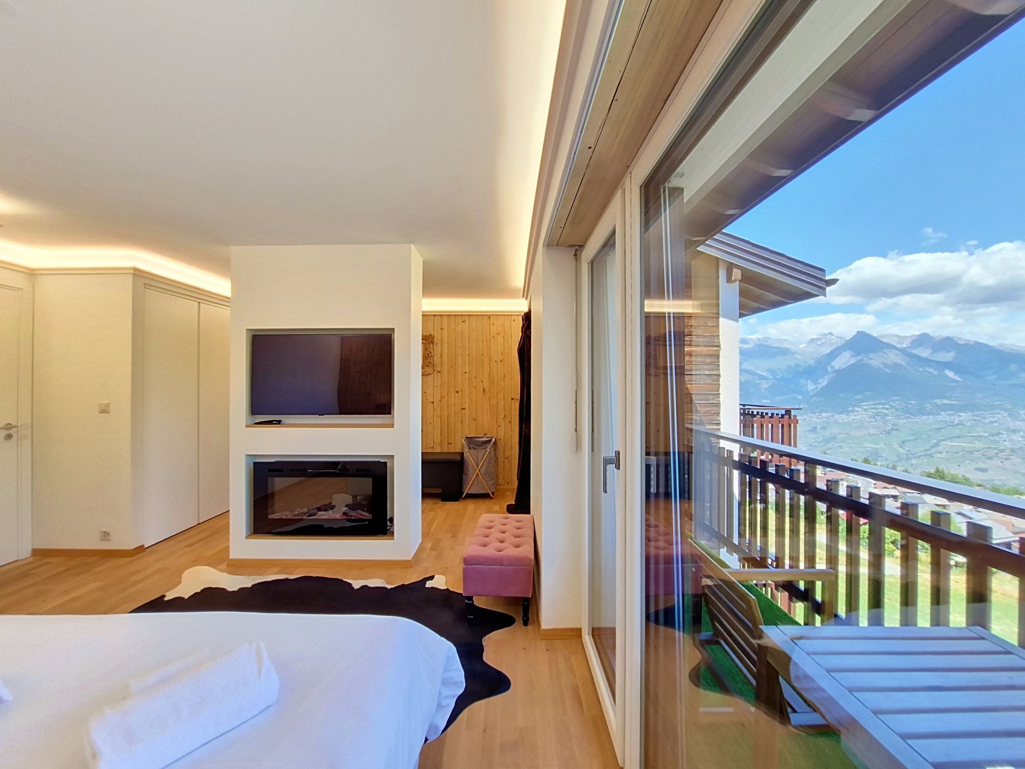 Een moderne slaapkamer met een bed, een flatscreen televisie, een open haard en een balkon met uitzicht op de bergen.