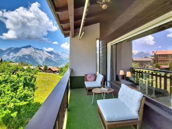 A balcony with a view of mountains, a sofa, a small table, and a chair.