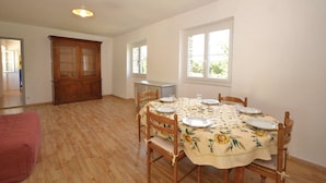 Ein Esszimmer mit einem runden Tisch, gedeckt für vier Personen, Holzstühlen, einer floralen Tischdecke, einem Holzschrank und einem Fenster, das für natürliches Licht sorgt.