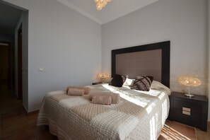 Ein Schlafzimmer mit einem großen Bett, zwei Nachttischlampen, einem Nachttisch und einer Tür zu einem anderen Raum.