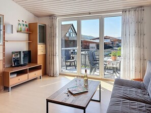 A living room with a TV, sofa, coffee table, and a view of a balcony with outdoor furniture. - Sonnige Aussichten - Obstbau Koch by Interhome (Bodman-Ludwigshafen)