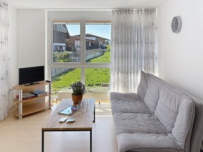 A living room with a sofa, a coffee table, a TV, and a view of a green landscape through a large window. - Ferienglück auf 2 Etagen - Obstbau Koch by Interhome (Bodman-Ludwigshafen)