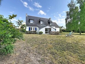 Ein Haus mit geneigtem Dach, einer Veranda und einem Rasen.