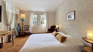 A bedroom with a large bed, a chair, a table, and a lamp.