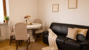 Un salon avec un canapé en cuir noir, des fauteuils beiges, une table de salle à manger ronde et une petite plante en pot.
