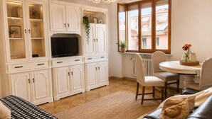 Un salon avec un téléviseur, des meubles blancs, une table à manger avec des chaises et une fenêtre donnant sur un beau paysage.