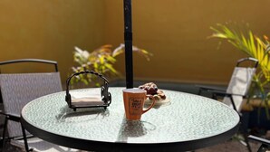 Una mesa redonda de vidrio con una silla metálica, una cesta de metal pequeña, una taza y un plato con pasteles.