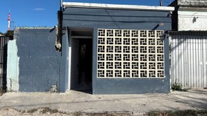 Un edificio con entrada protegida por un portón, una puerta visible y suelo de concreto.