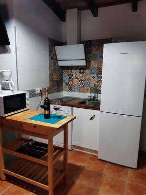 Cocina compacta con microondas, una botella de vino y una copa sobre una mesa de madera.