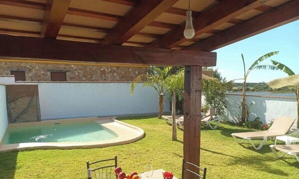 Un'area esterna coperta con piscina, sedie a sdraio e un tavolo apparecchiato per mangiare.