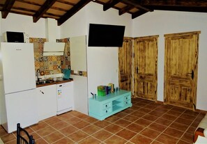 Una cocina compacta con refrigerador, microondas y salpicadero de azulejos. Se observa un gabinete color turquesa con libros y recipientes, además de puertas de madera al fondo.