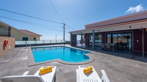 A swimming pool with two white lounge chairs and a yellow towel, a covered patio area, and a view of the sea. - Kaya Canhas by LovelyStay (Poiso)