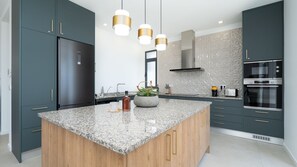 A modern kitchen with a central island, stainless steel appliances, and pendant lighting. - Papaya Villa by LovelyStay (São Gonçalo)