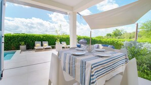 An outdoor patio with a table set for dining, surrounded by chairs, a pool, and a hedge. - SeaRock – Elegant Villa with Private Pool and Tropical Garden at Le Diamant (LE DIAMANT)