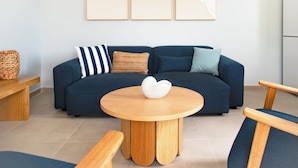 A modern living room with a dark blue sofa, a round wooden coffee table, and three wall-mounted abstract art pieces. - SeaRock – Elegant Villa with Private Pool and Tropical Garden at Le Diamant (LE DIAMANT)