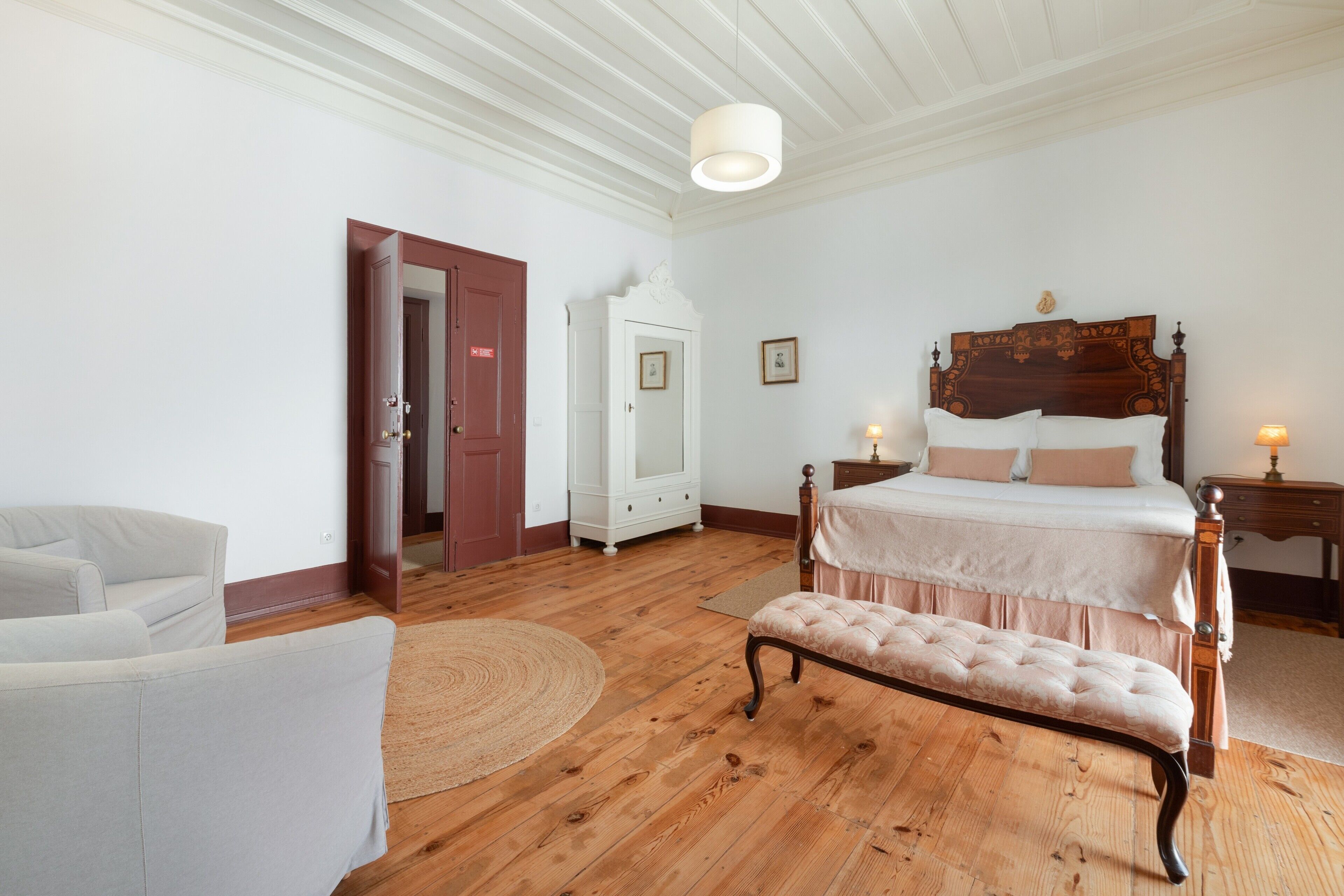 Een slaapkamer met een houten bed, een bankje, een witte inbouwkast en een deur.