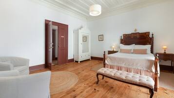 Een slaapkamer met een houten bed, een bankje, een witte inbouwkast en een deur.