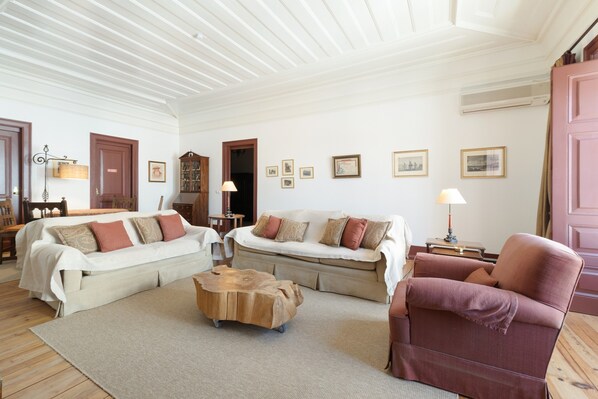 A living room with two sofas, a coffee table, and a red armchair. There are framed pictures on the walls and a wooden cabinet.