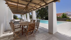 Une terrasse extérieure avec une table et des chaises en bois, une piscine en arrière-plan et un ciel dégagé.