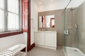 A bathroom with a glass shower enclosure, a white sink with a mirror above it, and a checkered floor pattern.