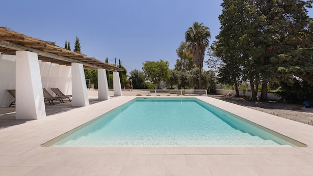 Une piscine rectangulaire à l’eau claire, entourée de piliers blancs et surmontée d’une pergola.