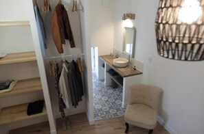 A bathroom with a sink, mirror, and hanging clothes rack.