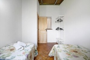 A small room with two beds, a wooden door, and a white shelf with hangers.