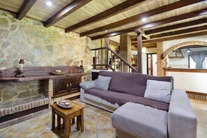 A stone wall, wooden beams, a sofa, a table, and a staircase.
