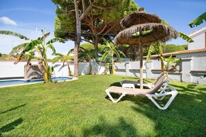 Patio con piscina, una silla de descanso y un quiosco techado de paja.