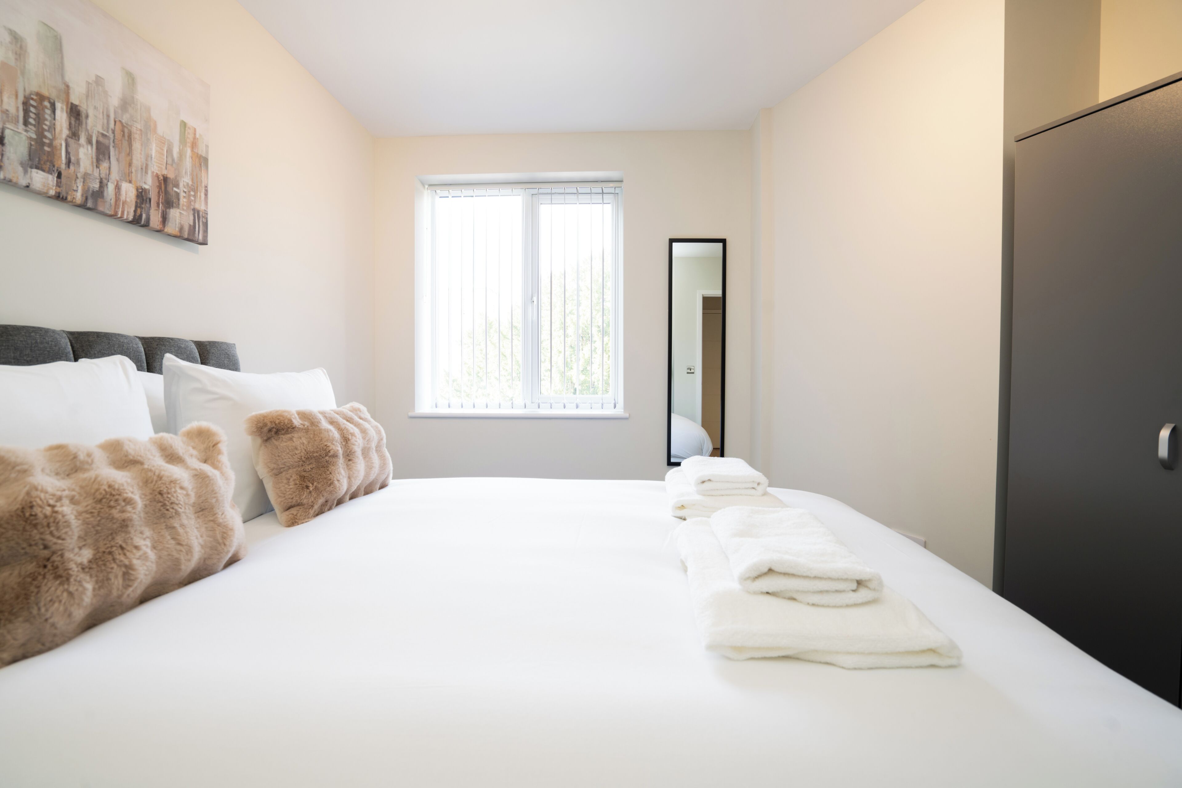 Ein Hotelzimmer mit einem großen Bett, einem Fenster mit Jalousien, einem Spiegel und einem Kleiderschrank.