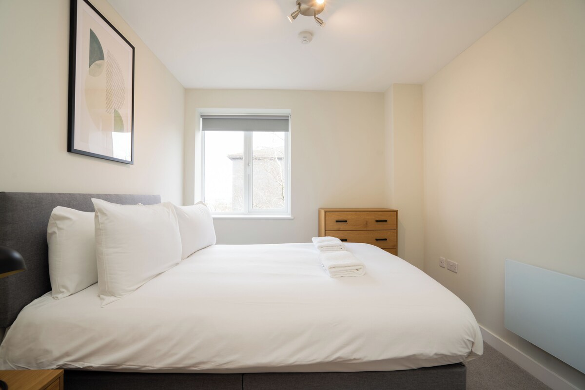 A bedroom with a bed, a window, a bedside table, and a wall-mounted artwork.