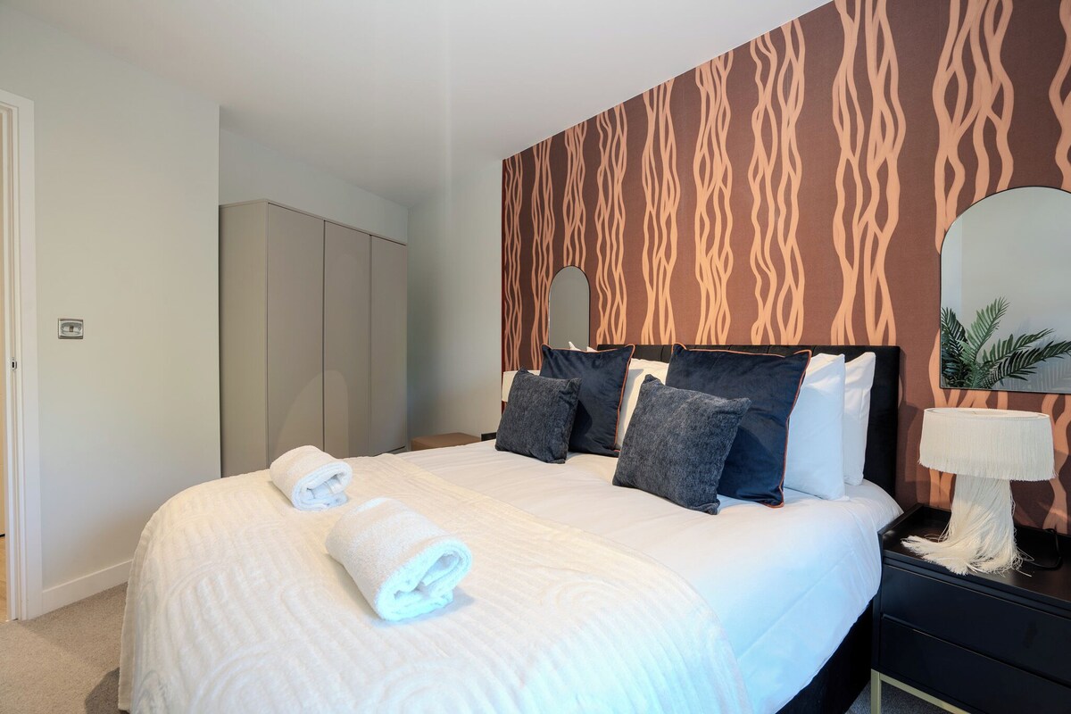 A neatly made bed with rolled towels, a bedside lamp, and a mirror on the wall.