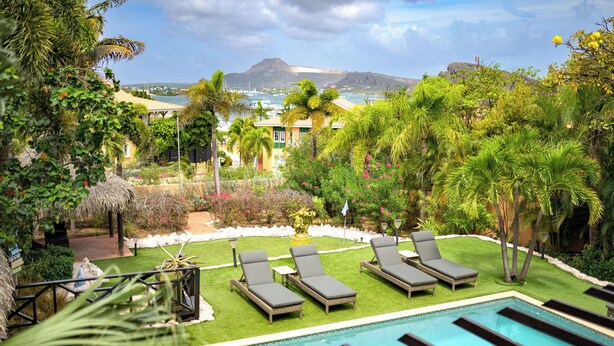 Ein Poolbereich mit Liegestühlen, einem kleinen Garten und Blick auf das Meer.