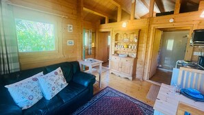 Ein Holzblockhaus-Interieur mit einer Couch, einem kleinen Tisch, einem Schrank und einem Essbereich.